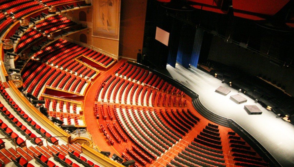 The empty house of The Colosseum, red seats sweeping toward the thrust stage.